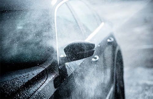 A black vehicle being sprayed with the automatic car wash system
