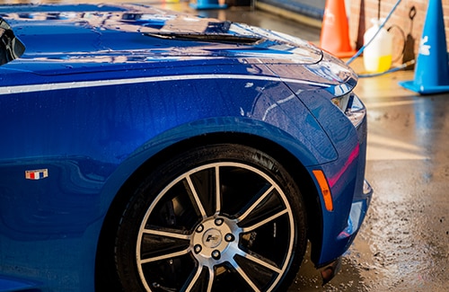 The side of a blue sports car being pre-rinsed
