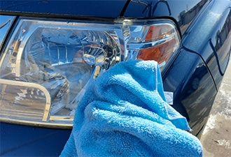 A blue towel being used to wipe down the headlight of a truck