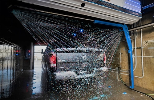 The rear of a grey truck being sprayed by the automatic car wash system in a wash bay